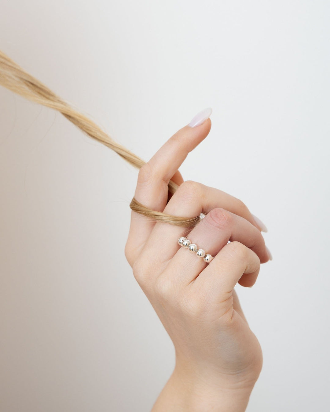 anello elasticizzato grande argento indossato su mano con ciocca di capelli tra le dita